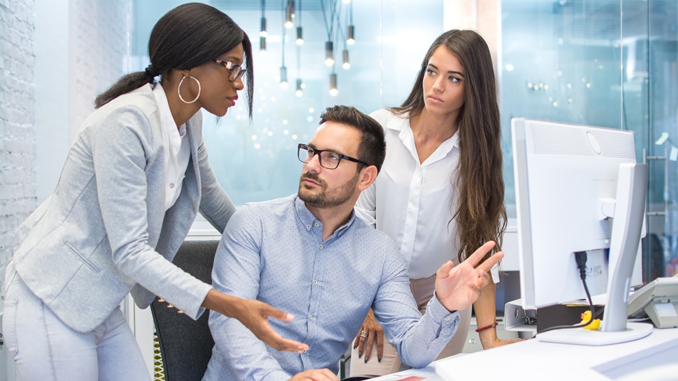 3 people at work desk involved in a dispute, one is attempting to intervene