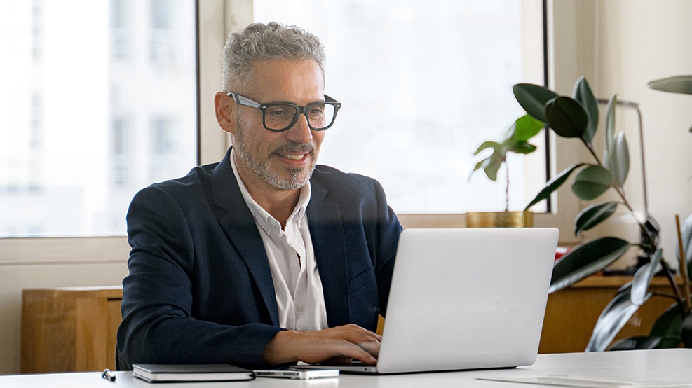 man with glass at laptop behind a desk